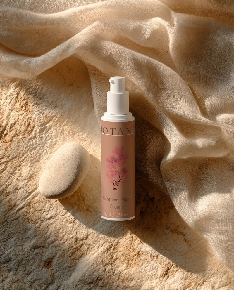 BOTANĒ Sensitive Night Cream pump bottle on textured stone with a smooth white pebble and draped linen in warm sunlight. primary product image