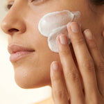 Close-up of a hand smoothing a thick layer of white BOTANĒ facial cream onto a cheek. thumbnail 3
