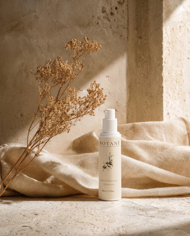 BOTANĒ Retinol Alternative Moisturiser pump bottle on textured stone with draped linen and dried flowers in warm sunlight. product image
