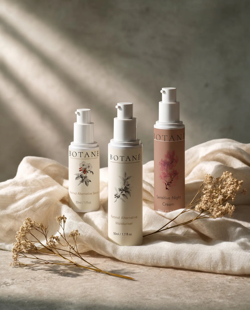 Three BOTANĒ skincare pump bottles—Retinol Alternative Serum, Moisturiser, and Sensitive Night Cream—on draped linen with dried flowers.
